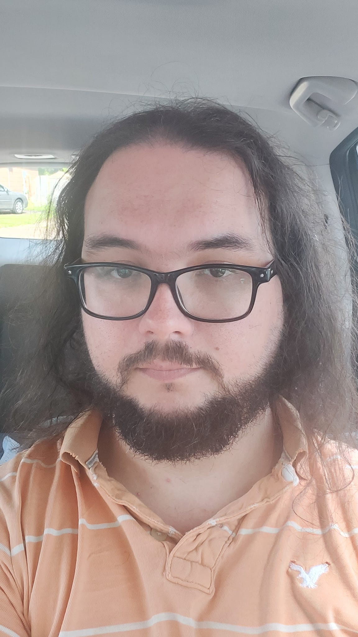 A man with long dark hair sits in a car, he looks sad and tired, photo 2